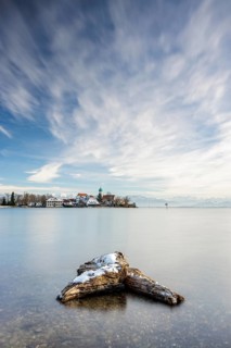 A peaceful lake with a log in the foreground with picturesque St George's Church on the lakeshore