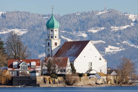 St George's Church with green tower in front of snow-covered Pfänder, surrounded by village houses,