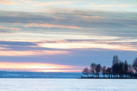A peaceful sunset over a lake with silhouetted trees and a colourful evening sky, harbour,