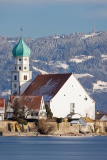St George's Church with green tower in front of snow-covered Pfänder, surrounded by village houses,