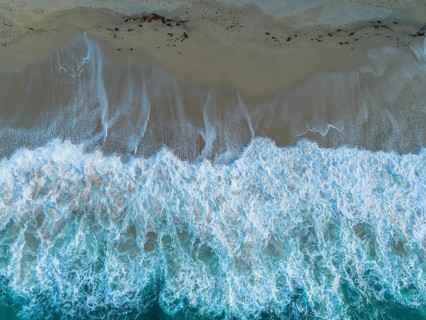 A top down view of the golden sand Rotonda Beach in Tropea with turquoise water and waves crashing