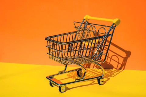 Empty shopping trolley cart on colorful orange yellow background. Copy space for your text. Online