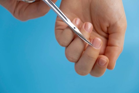 Stylish nude beige female nails using scissors on blue background. Modern trendy stylish Beautiful