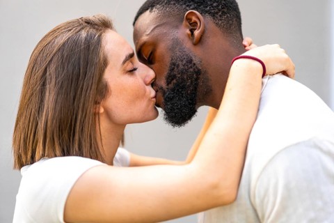 Side view close-up of a multiracial couple of lovers dressed in white kissing tenderly and