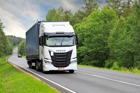 White Iveco S-Way truck pulls curtainside semi trailer uphill along highway 52 on a day of summer.