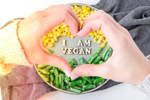 Female hands in shape of heart love I AM VEGAN text in plate. Veganism, vegetarian healthy