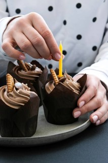 Female hands making Delicious chocolate cupcakes with cream on dark background. Three chocolate
