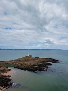 A view of the Mumbles Lighthouse in Swansea Bay at low tide with algae and rocks in the foreground