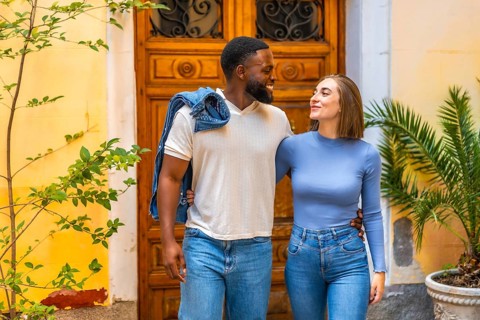 Multi-ethnic couple leaving the house together with a smile, embraced from behind