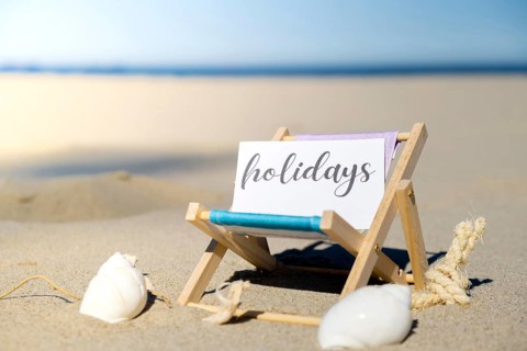 HOLIDAYS text on paper greeting card on background of beach chair lounge summer vacation decor.