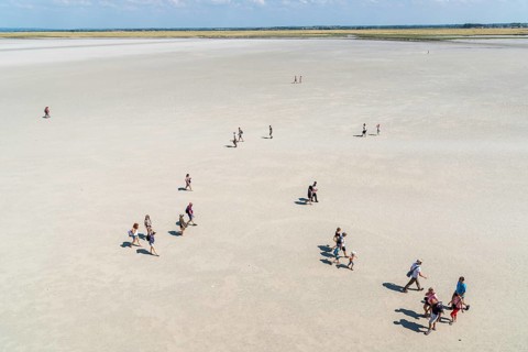 Mont Saint Michel, France, July 25, 2018: Group of hikers in the bay at low tide, Europe