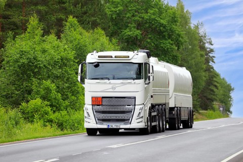 White Volvo FH tank truck transports gasoline fuel, ADR code 33-1203, on rural highway on a day of