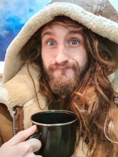 Portrait shot of a funny young man with a camping tin tea cup in his hand, looking at camera and