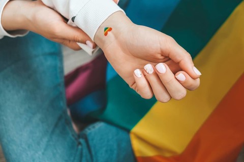 Closeup of young caucasian millennial hippie woman with a rainbow flag in heart shape painted in