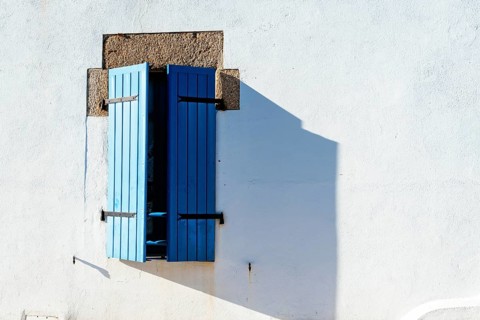Old window with wooden blue painted shutters on white painted wall