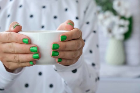 Manicured female hands with stylish green nails holding cup of coffee. Take a break for coffee