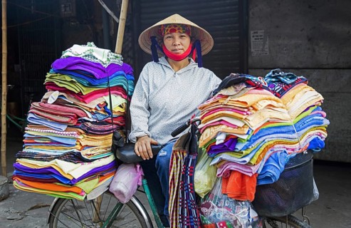 Vietnamese woman with nón lá conical hat selling textile and clothes from bicycle in the city Ninh
