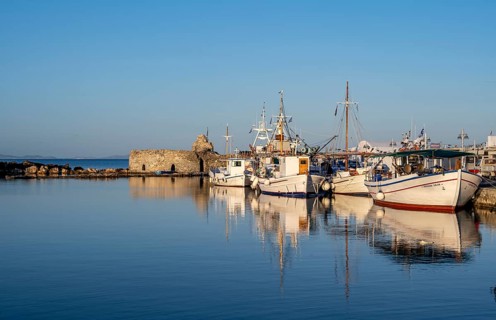 Fishing boats in the harbour and ruins of the Venetian castle, reflected in the sea, at sunset,