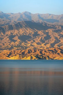 Blue Toktogul reservoir between dry mountain landscape, hilly mountains in the evening light,