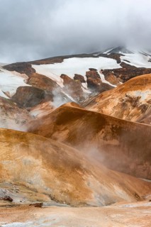 Hot springs and steaming stream between colourful rhyolite mountains with snowfields, Hveradalir