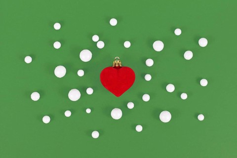 Red heart shaped Christmas tree bauble surrounded by snowballs on green background
