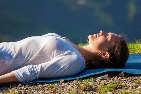 Woman relaxes in yoga relaxation asana Savasana, corpse pose outdoors in Himalayas. Himachal