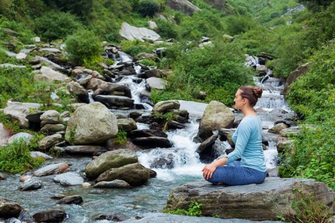 Woman in Hatha yoga asana Padmasana outdoors at tropical waterfall