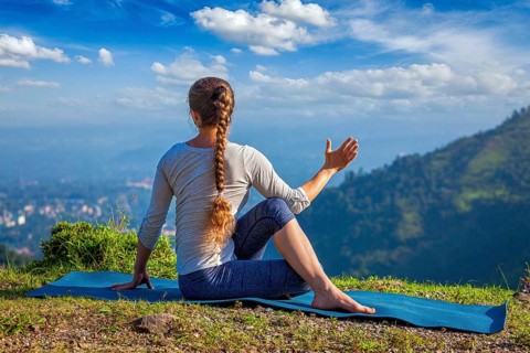 Hatha yoga outdoors, woman doing yoga asana Parivrtta Marichyasana or ardha matsyendrasana, seated