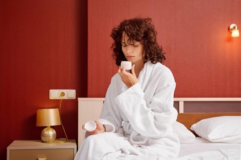 Woman in bathrobe opened jar of cream and inhales its fresh aroma