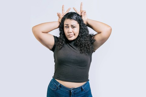 Funny girl making horns gesture with their fingers, gesture of betrayal. Funny young woman making