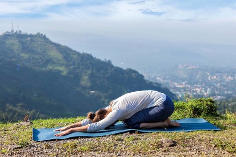 Sporty fit woman practices yoga asana Balasana, child pose outdoors in mountains