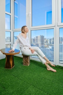Barefoot young woman sits on the balcony of her new apartment and admires the view of the city from