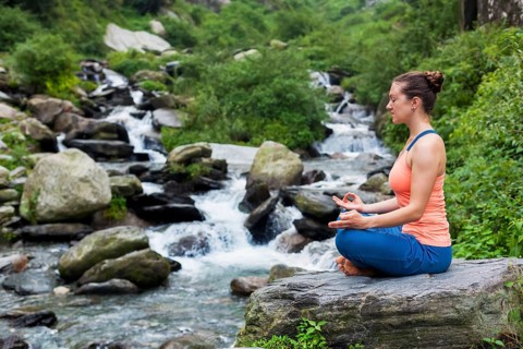 Woman meditating in Hatha yoga asana Padmasana outdoors at tropical waterfall