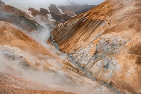 Steaming stream between colourful rhyolite mountains and snowfields, Hveradalir geothermal area,