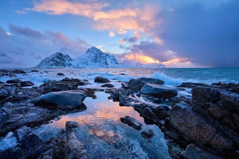 Beach of Norwegian sea on rocky coast in fjord on sunset in winter. Vareid beach, Lofoten islands,