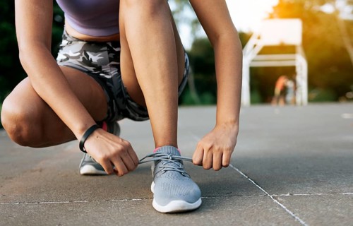 Sport girl tying her shoe laces in a park. Runner girl tying her running shoes in a park with space