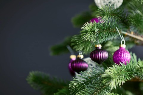 Close up of beautiful purple glass tree bauble with decorated Christmas tree with other seasonal