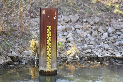 Yellow metric flood level marker in river with low water level