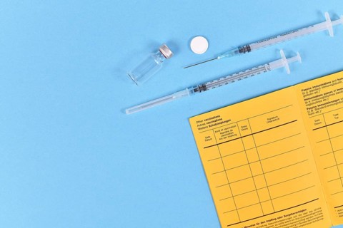 Vaccine concept with syringe, vial and yellow international certificate of vaccination on blue