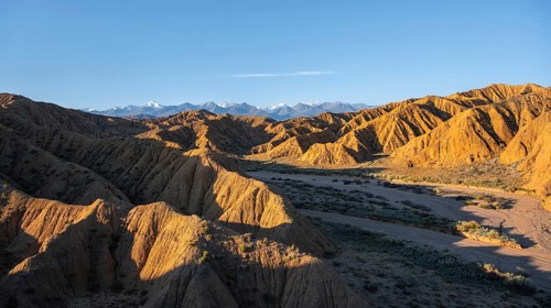 Canyon through a landscape of eroded hills at sunrise, Badlands, white mountain peaks of the Tian