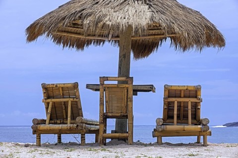 Relaxing bamboo deck chairs with parasol on white sandy beach looking towards ocean at Pantai