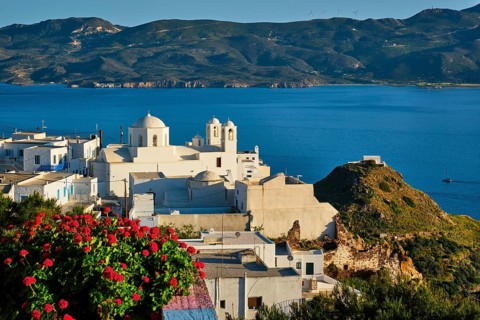 Picturesque scenic view of Greek town Plaka on Milos island over red geranium flowers and Orthodox
