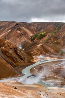 Bridge and steaming streams between colourful rhyolite mountains in the Hveradalir geothermal area,