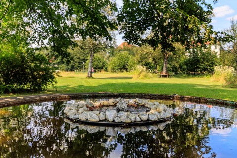 Small fountain and water bowl with stones under trees, Schlehdorf Monastery, Bavaria, Germany,