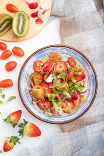 Vegetarian fruits and vegetables salad of strawberry, kiwi, tomatoes, microgreen sprouts on white
