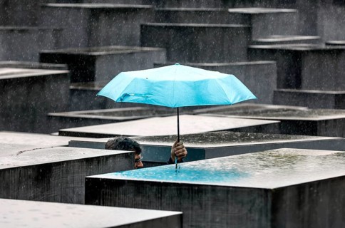 A visitor to the Memorial to the Murdered Jews of Europe protects himself from heavy rain with an