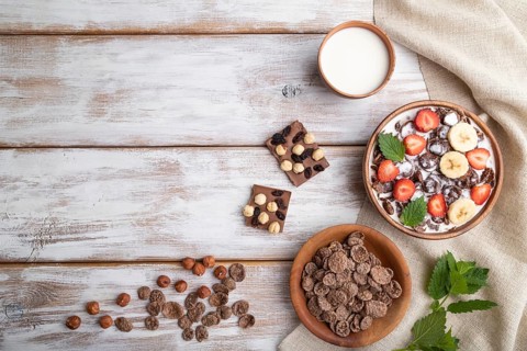Chocolate cornflakes with milk and strawberry in wooden bowl on white wooden background and linen
