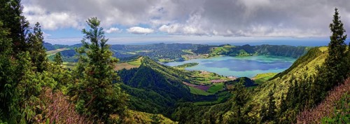 Wide panorama of the crater lake Lagoa Azul surrounded by lush green hills and clouds in the sky,