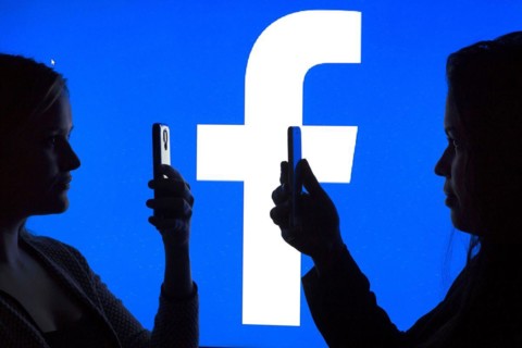 Silhouettes of two woman with smartphones in front of Facebook logo, 12.01.2016