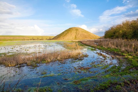 Silbury Hill ancient neolithic manmade chalk mound in Avebury, Wiltshire, England with flood water